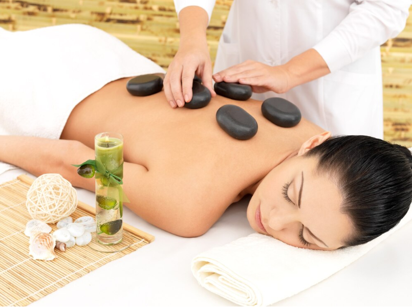 Hands placing smooth, warm stones on a back, symbolizing deep muscle relaxation and warmth provided by hot stone massage.